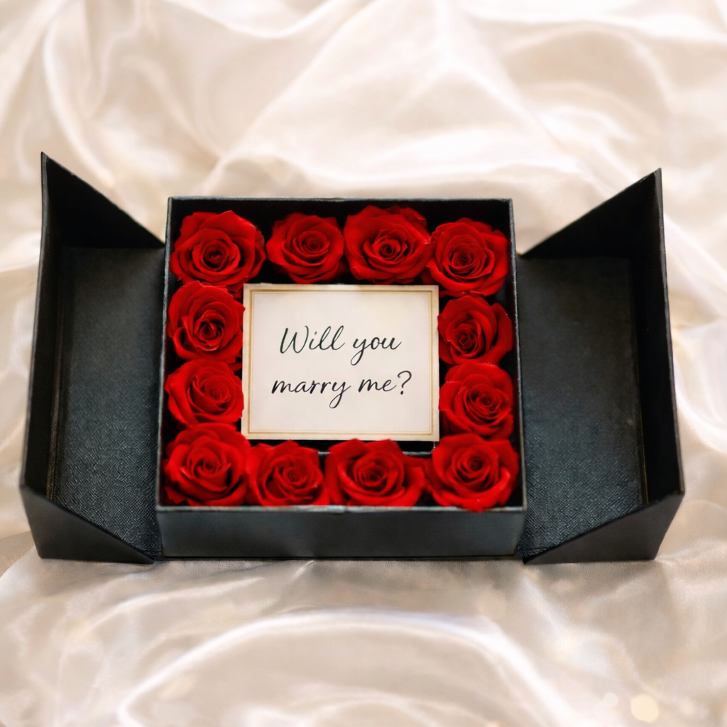 Box of red roses with a 'Will you marry me?' card on a white fabric background