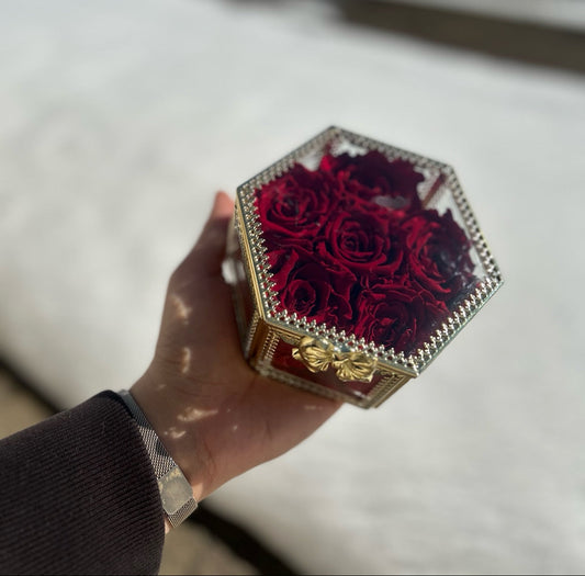 Hand holding a decorative box with a red rose design against a blurred outdoor background
