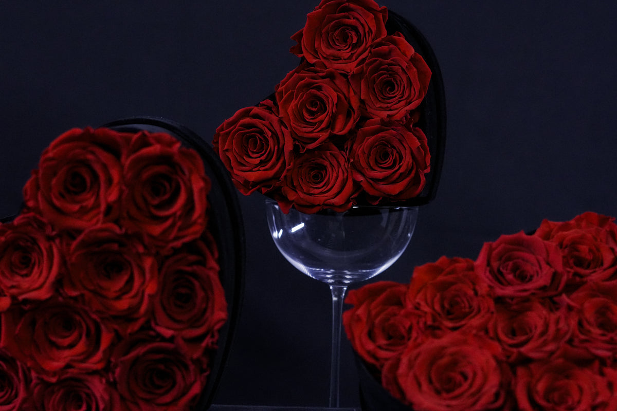 Red roses in heart-shaped boxes and a wine glass on a dark background